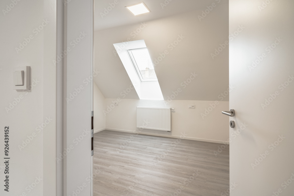 A room with a slanted ceiling and a skylight, light-colored laminate flooring, white walls, and an open door, showcasing a clean and modern interior. A room with a slanted ceiling and a skylight, light-colored laminate flooring, white walls, and an open door, showcasing a clean and modern interior.