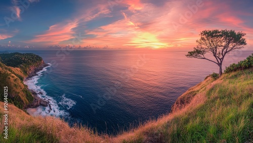 Stunning panorama of rugged coastline at golden hour. Lone tree silhouetted against vibrant pink and orange sky. Waves crash on rocky shore below grassy cliffs