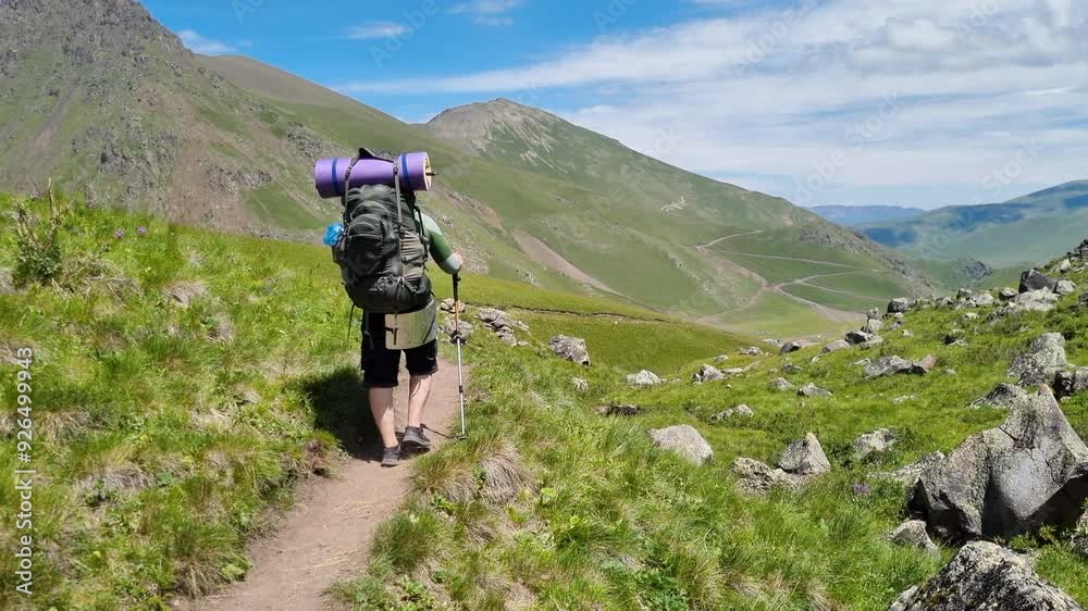 Hiker walking on trail in mountains carrying backpack and trekking poles Hiker walking on trail in mountains carrying backpack and trekking poles