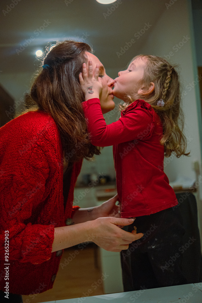 A young mother and her beautiful daughter are making Christmas cookies. The mother and daughter, wearing red sweaters, are making New Year's style cookies, cutting out different shapes with molds A young mother and her beautiful daughter are making Christmas cookies. The mother and daughter, wearing red sweaters, are making New Year's style cookies, cutting out different shapes with molds