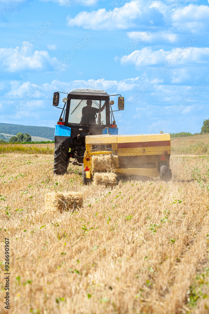 Close-up of hay baling with a tractor using a baler on a cloudy summer day, a large bale comes out of the baler. Close-up of hay baling with a tractor using a baler on a cloudy summer day, a large bale comes out of the baler.