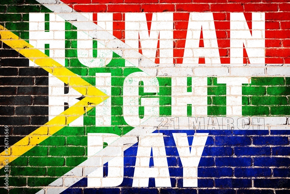 Fototapeta premium The national Human right day text on the flag of South Africa depicting in paint colors on an old brick wall. Flag banner on brick wall background