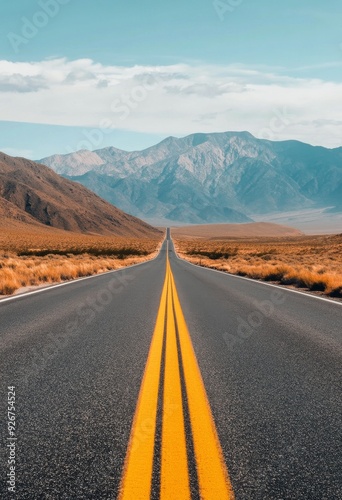 Long stretch of highway leading towards mountains under a clear blue sky