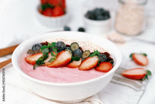 Presented by fruits putting yogurt toppings with strawberry, berry, oats, raisins and chia seed decorated by peppermint in white blow. Pink background. Set of healthy dairy product choice. Pecuniary.