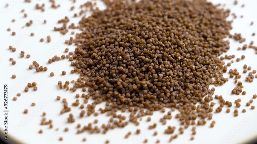 Brown dry buckwheat couscous grains falling on a ceramic plate. Uncooked food. Top view. Slow motion Brown dry buckwheat couscous grains falling on a ceramic plate. Uncooked food. Top view. Slow motion
