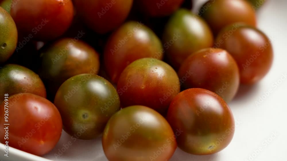 Ripe sweet kumato cherry tomatoes with dark green and red peel on a matte kitchen plate close up. Rotation Ripe sweet kumato cherry tomatoes with dark green and red peel on a matte kitchen plate close up. Rotation