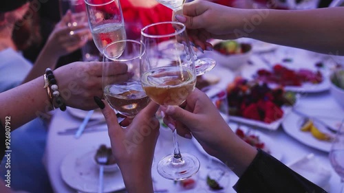 Group of guests celebrate and raise glasses, cheering with alcohol glasses with wine and champagne in the restaurant on corporate christmas birthday party event or wedding celebration, luxury event