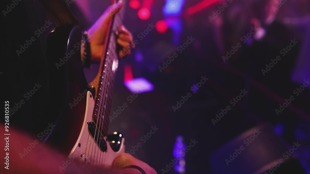 Concert view of an electric guitar player with vocalist and rock band performing in club, male musician guitarist on stage with audience in a crowded concert hall arena, live music show, slow motion
