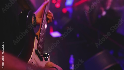 Concert view of an electric guitar player with vocalist and rock band performing in club, male musician guitarist on stage with audience in a crowded concert hall arena, live music show, slow motion
