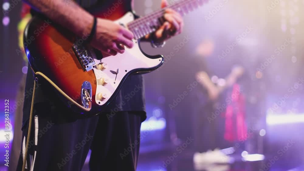 Concert view of an electric guitar player with vocalist and rock band performing in club, male musician guitarist on stage with audience in a crowded concert hall arena, live music show, slow motion

