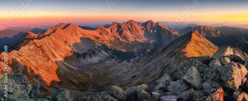Panoramic view of Tatra Mountains at sunrise, capturing golden hour light on summer peaks and autumn foliage, with red hues on rocky landscapes, offering a breathtaking and detailed natural scene.
