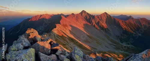 Panoramic view of Tatra Mountains at sunrise, capturing golden hour light on summer peaks and autumn foliage, with red hues on rocky landscapes, offering a breathtaking and detailed natural scene.