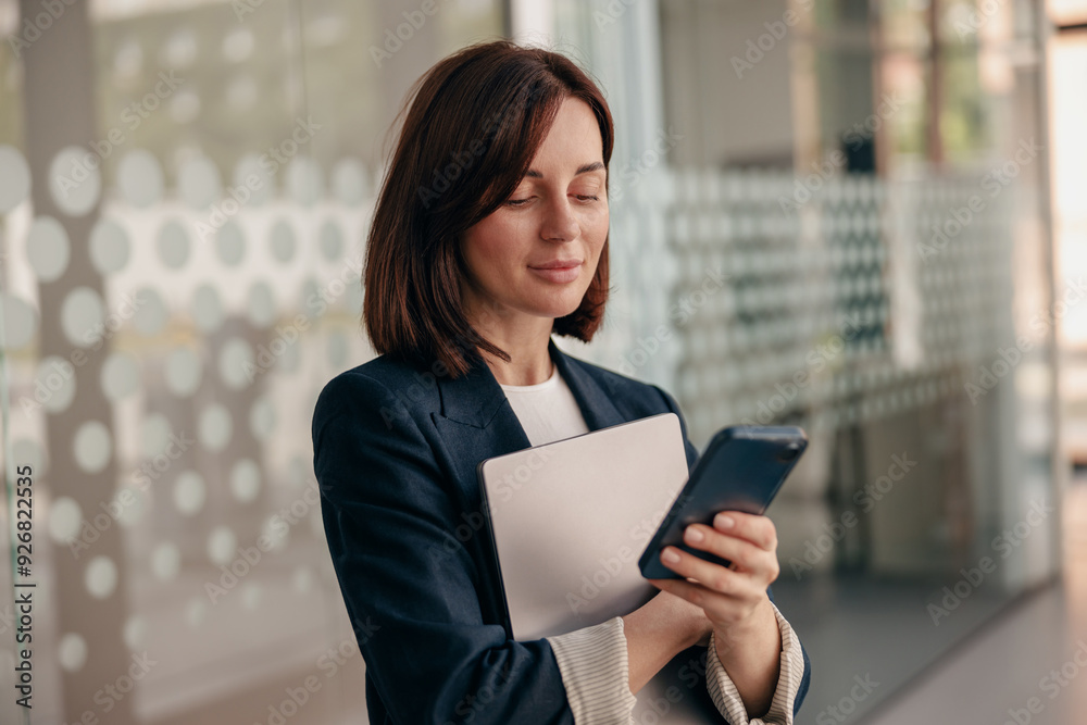 Confident businesswoman is focused on using her smartphone in a modern office setting Confident businesswoman is focused on using her smartphone in a modern office setting