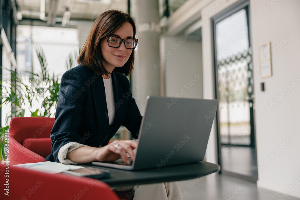 A businesswoman is deeply focused as she works on her laptop in a modern office environment A businesswoman is deeply focused as she works on her laptop in a modern office environment