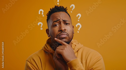 Thoughtful Black Man Contemplating with Question Marks, Puzzled Expression on Orange Background photo