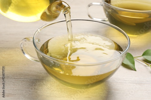 Pouring refreshing green tea into cup at wooden table, closeup