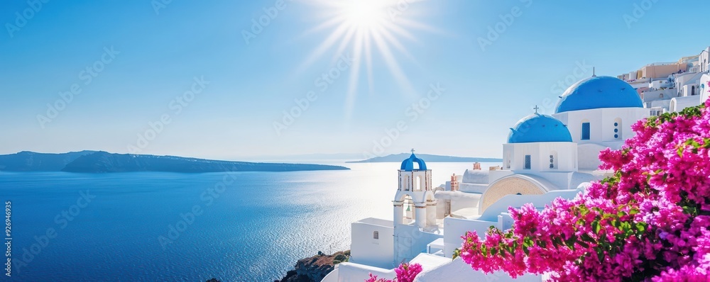 Naklejka premium Whitewashed Greek island architecture with blue domes and blooming pink flowers against a bright blue sky and sparkling sea.