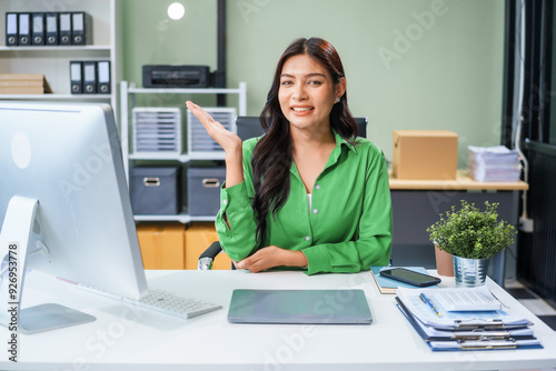 An Asian businesswoman sits at the table in her office, working as an accountant. She uses a computer with a smile, feeling happy and content with her work.