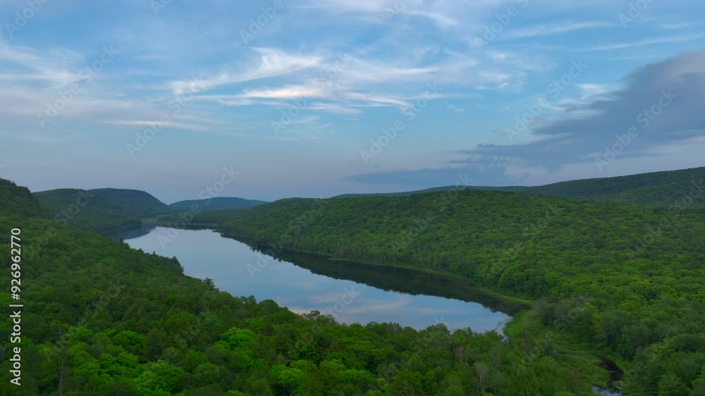 A breathtaking view of Lake of the Clouds at sunset during July, captured by drone footage in the Porcupine Mountains, Upper Peninsula, Michigan. The tranquil lake reflects the serene sky. A breathtaking view of Lake of the Clouds at sunset during July, captured by drone footage in the Porcupine Mountains, Upper Peninsula, Michigan. The tranquil lake reflects the serene sky.