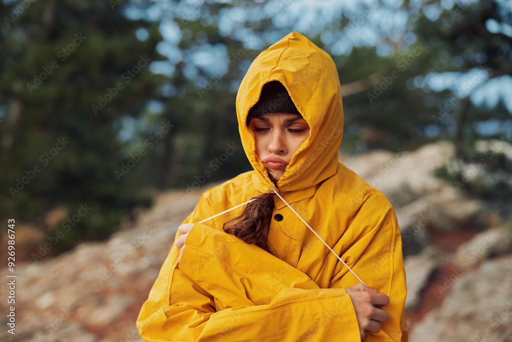 A serene young woman in a vibrant yellow raincoat enjoying the beauty of nature on a rocky hill A serene young woman in a vibrant yellow raincoat enjoying the beauty of nature on a rocky hill