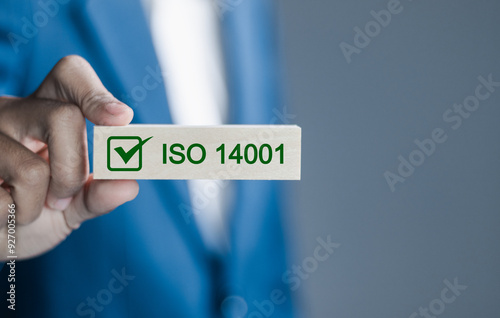 ISO 14001 concept. Businessman hold wooden block with icon of ISO 14001 certified for environmental management systems (EMS). Identify, control and reduce the environmental impact of activities. photo