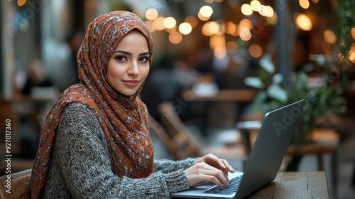 Young Woman in Hijab Working on Laptop at a Cozy Cafe with Warm Ambient Lights photo