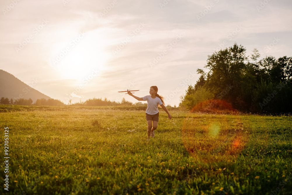 Cheerful little girl runs with toy plane on background beautiful warm sunset in mountains. Funny child dream to fly. Kid become an airplane pilot. Flight dream concept. Playful preteen playing aviator Cheerful little girl runs with toy plane on background beautiful warm sunset in mountains. Funny child dream to fly. Kid become an airplane pilot. Flight dream concept. Playful preteen playing aviator