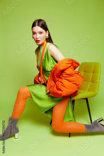 High fashion portrait of young asian woman on light green background. Orange down jacket, orange tights, light green dress, orange tie photo