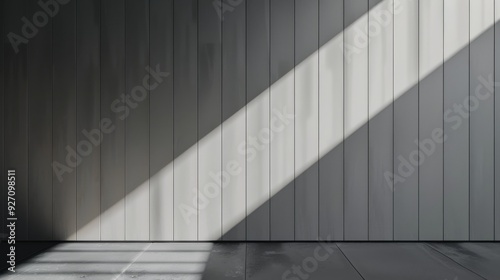 Sunlight streams through a window  casting a diagonal shadow across a grey wooden wall  highlighting the vertical lines of the wood. The floor is made of dark concrete  also reflecting the light in su