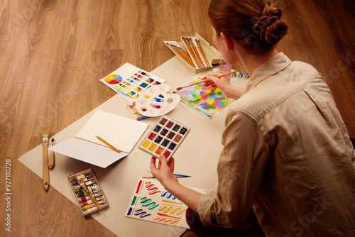 Woman painting with watercolors surrounded by art supplies