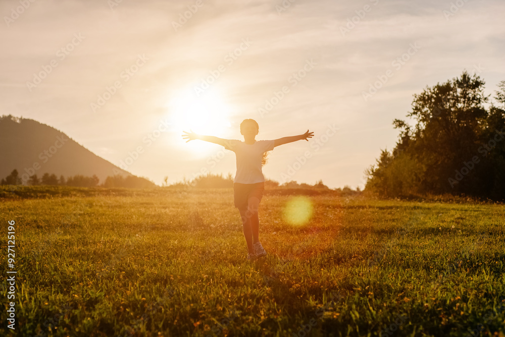 Child waving hands in summer park. Forest on bright light background. Cloudy sunny sky. Playful preteen girl running on grass field of dry grass during beautiful warm sunset in mountains Child waving hands in summer park. Forest on bright light background. Cloudy sunny sky. Playful preteen girl running on grass field of dry grass during beautiful warm sunset in mountains