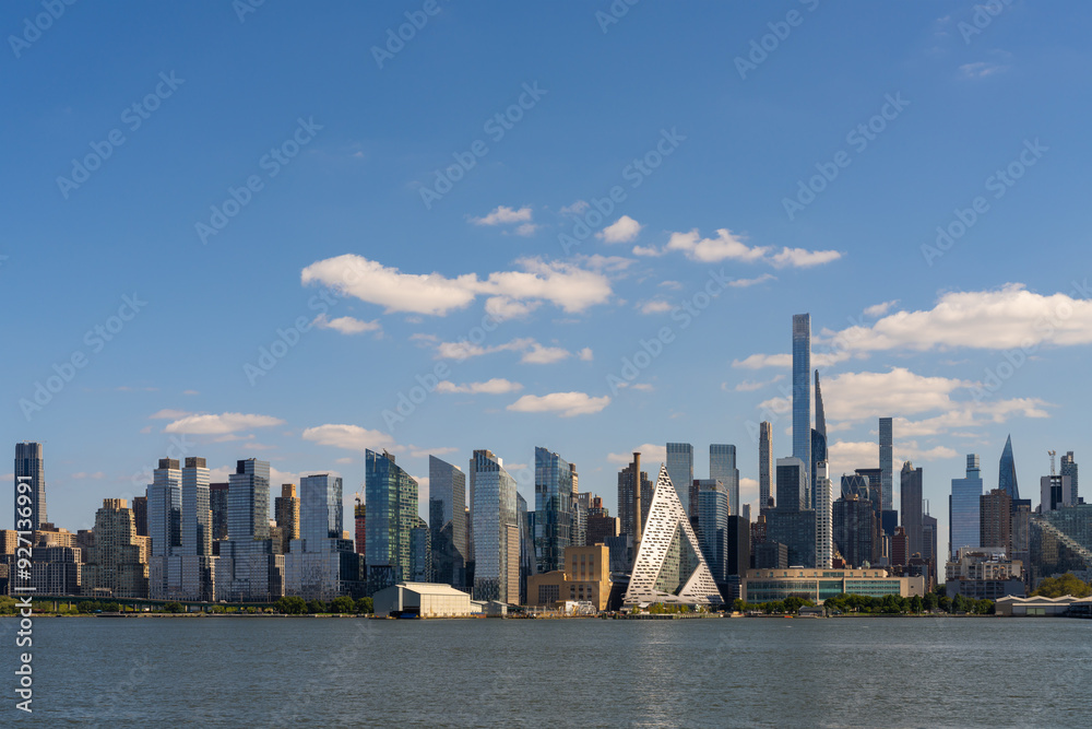 Naklejka premium Manhattan waterfront cityscape with modern skyscrapers under clear blue sky.