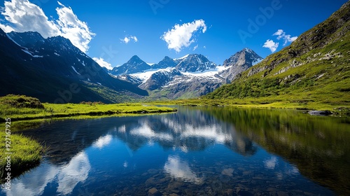 Breathtaking mountain landscape reflecting perfectly in a serene lake under a clear blue sky with fluffy white clouds.