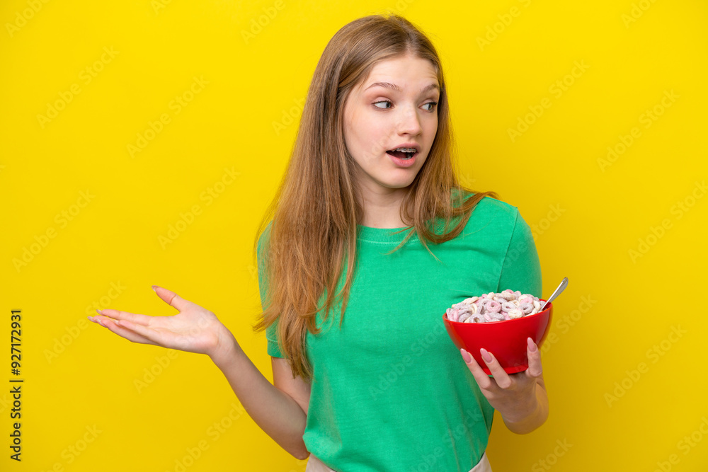 Teenager Russian girl holding bowl of cereals isolated on yellow background with surprise expression while looking side Teenager Russian girl holding bowl of cereals isolated on yellow background with surprise expression while looking side