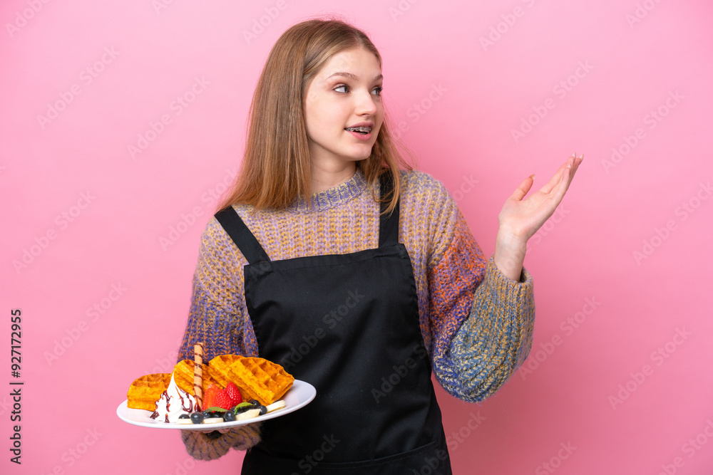Teenager Russian girl holding a waffles isolated on pink background extending hands to the side for inviting to come Teenager Russian girl holding a waffles isolated on pink background extending hands to the side for inviting to come