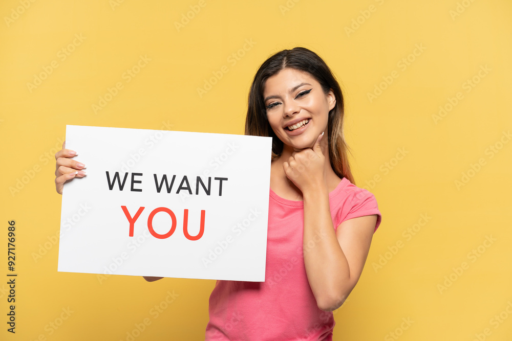 Young Russian girl isolated on yellow background holding We Want You board and shouting Young Russian girl isolated on yellow background holding We Want You board and shouting
