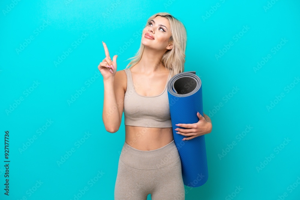 Sport woman going to yoga classes while holding a mat isolated on blue background pointing up a great idea Sport woman going to yoga classes while holding a mat isolated on blue background pointing up a great idea