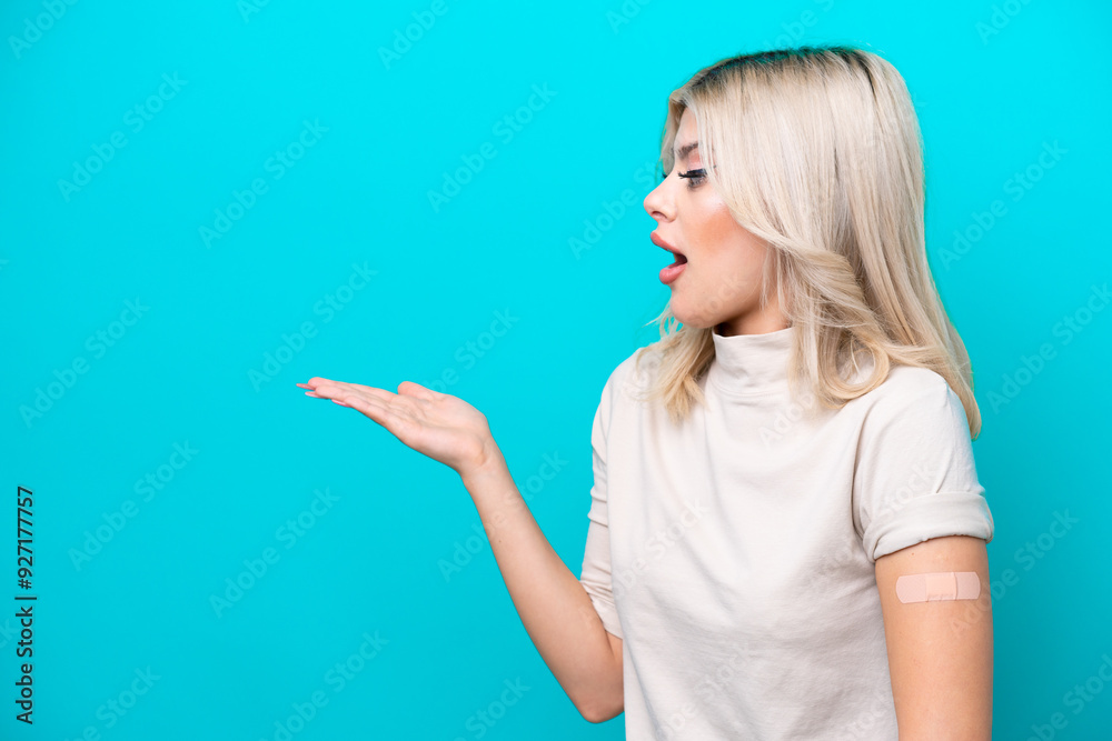 Young Russian woman wearing band aid isolated on blue background with surprise facial expression Young Russian woman wearing band aid isolated on blue background with surprise facial expression
