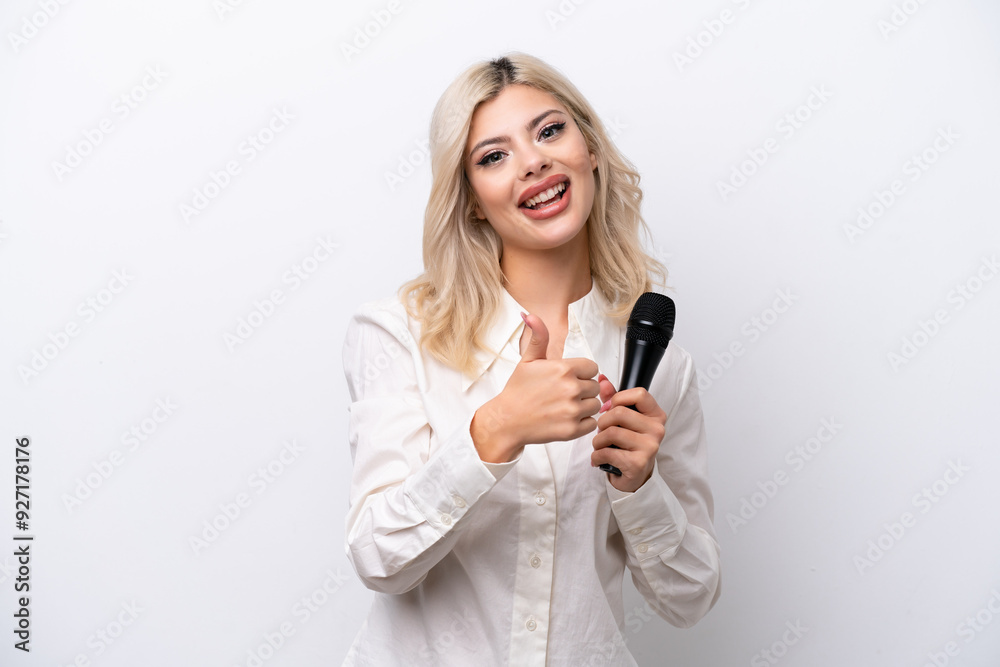 Young singer woman picking up a microphone isolated on white background giving a thumbs up gesture Young singer woman picking up a microphone isolated on white background giving a thumbs up gesture