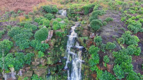 Yorkshire moor's magnificent waterfall, aerial footage: water cascades over boulders into a deep blue pool with hikers.