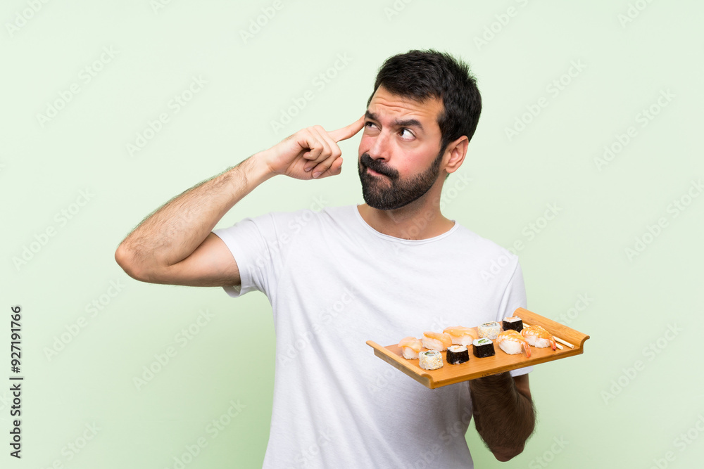 Young handsome man with sushi over isolated green wall having doubts and thinking Young handsome man with sushi over isolated green wall having doubts and thinking