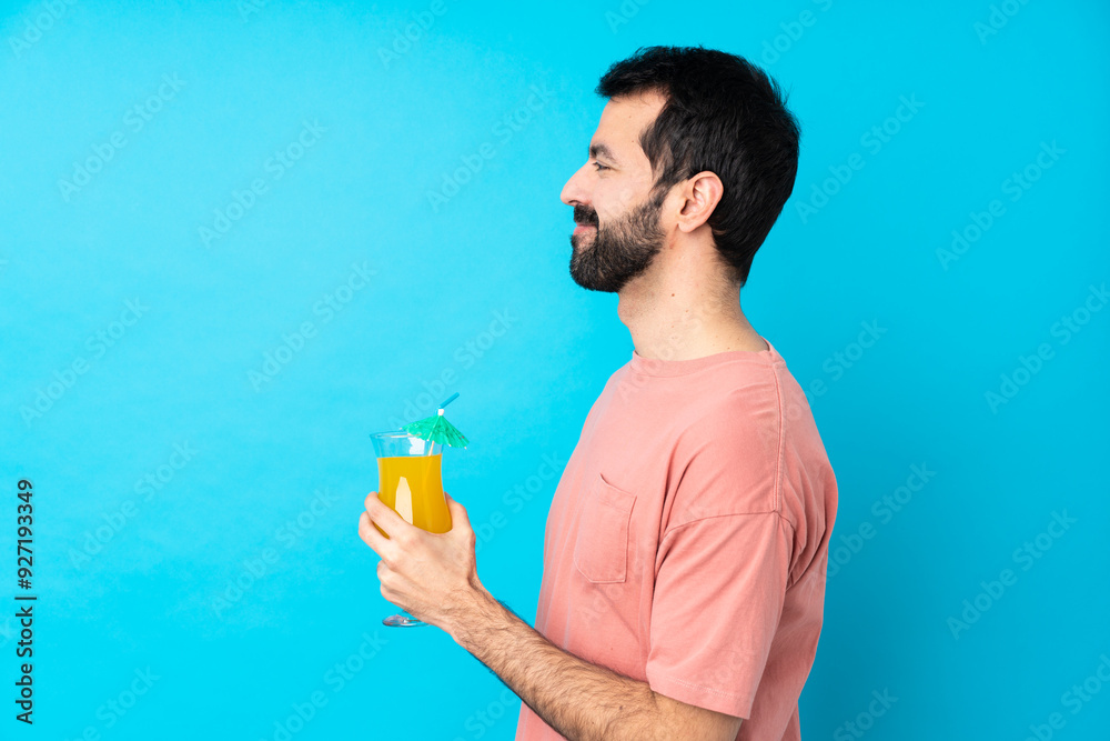 Fototapeta premium Young man over holding a cocktail over isolated blue background in lateral position