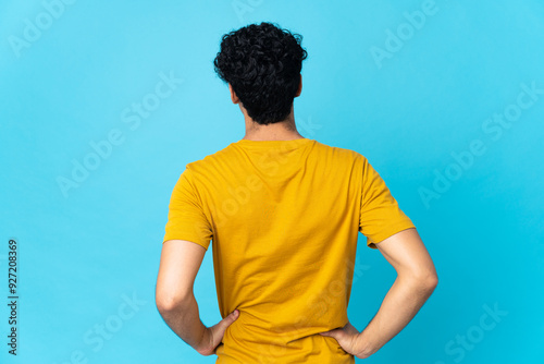 Young Venezuelan man isolated on blue background in back position