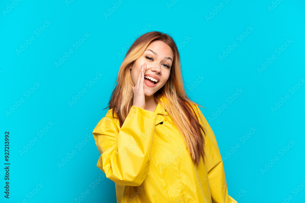 Teenager girl wearing a rainproof coat over isolated blue background shouting with mouth wide open Teenager girl wearing a rainproof coat over isolated blue background shouting with mouth wide open