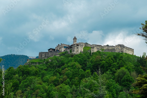 Panoramic view Landskron Castle in Villach, Carinthia, Austria. Majestic fortress perched atop verdant forest covered hill. Imposing structure with fortified walls, towers and prominent church spire