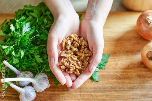 Walnuts in the hands of a woman over a wooden table, fresh parsley, onions, garlic. Fresh vegetables and herbs on a wooden board for making a salad or dinner, walnuts healthy and healthy food