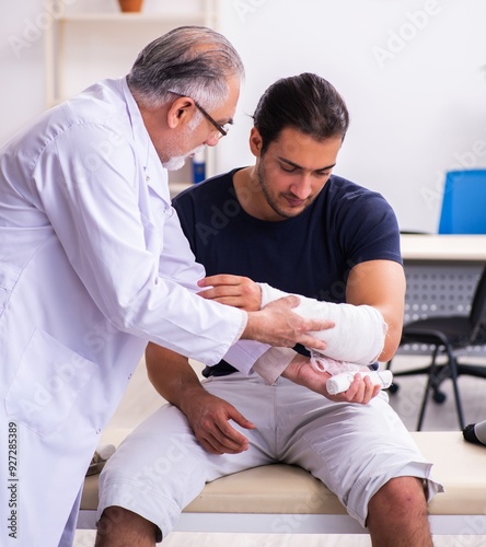 Obraz na płótnie Young injured man visiting experienced male doctor traumatologis w salonie