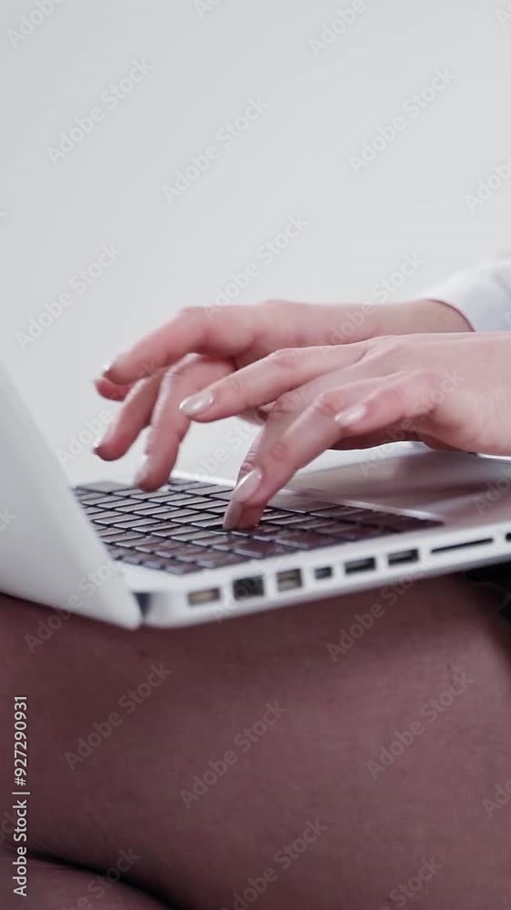 Young female is typing on a laptop. White laptop on woman's knees. Hands of a woman working on a modern gadget. Close-up. Slow motion. Vertical video Young female is typing on a laptop. White laptop on woman's knees. Hands of a woman working on a modern gadget. Close-up. Slow motion. Vertical video