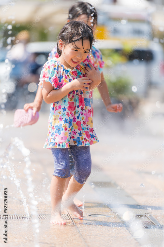 Naklejka premium 夏の広場の噴水で水遊びをする女の子