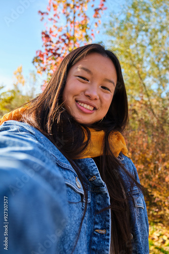 Young Asian woman smiling and taking a selfie in a park in autumn.
